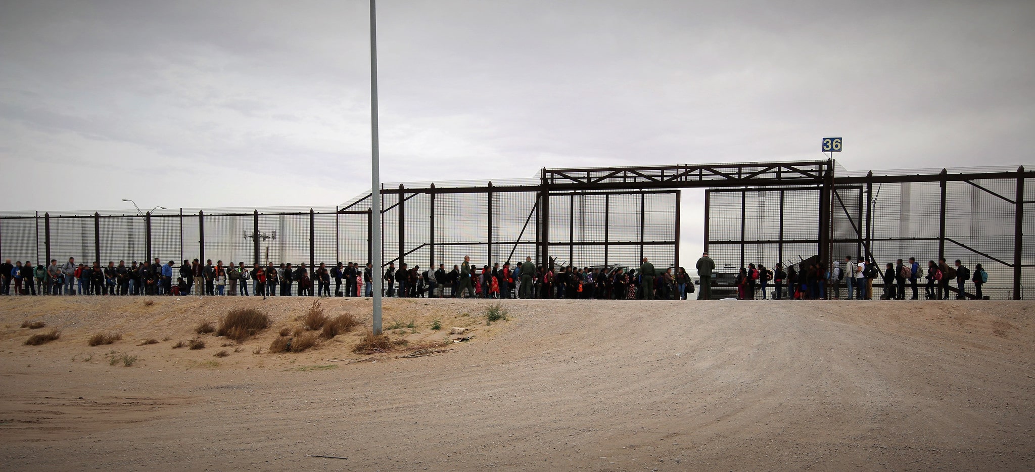 Migrantes centroamericanos esperando junto a la valla fronteriza entre México y Estados Unidos.